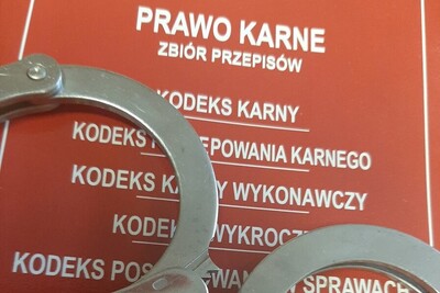 kajdanki położone na zbiorze przepisów z prawa karnego. zbiór prawa karnego jest w kolorze czerwonym z białymi napisami.  kajdanki koloru srebrnego.