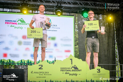 scena z podium. na miejscu 2 i 3 stoją mężczyźni, którzy zajęli te miejsca w biegu