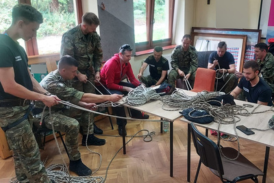 Funkcjonariusze KaOSG ćwiczą wiązania na linach, instruktarzu udziel im ratownik GOPR. Na stole znajdują się różnego rodzaju liny, uprzęże i karabińczyki.