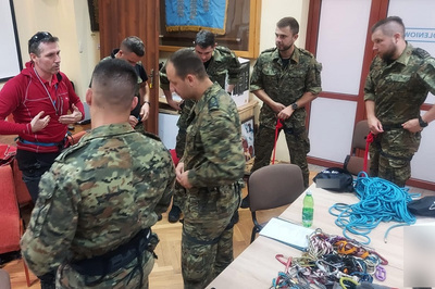 Funkcjonariusze KaOSG ćwiczą zakładanie uprzęży na sobie, instruktarzu udziela im ratownik GOPR. Na stole znajdują się różnego rodzaju liny, uprzęże i karabińczyki.