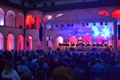 Dziedziniec Zamku Suskiego, wieczorna sceneria, czerwone i fioletowe światła nadają nastrój  publiczność siedzi pod sceną. na scenie gra orkiestra reprezentacyjna SG