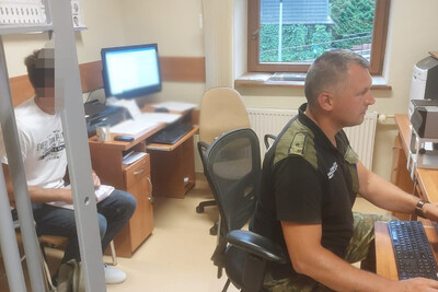 Funkcjonariusz SG siedzi przy biurku. za jego plecami siedzi zatrzymany Mołdawianin, który jest przesłuchiwany.