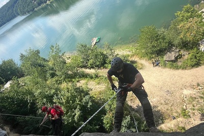 Na pionowej skale do wspinaczki, na linach wiszą funkcjonariusz SG i ratownik GOPR. na głowach mają kaski i wyposażeni są w niezbędny sprzęt wspinaczkowy. W tle widać taflę jeziora rożnowskiego