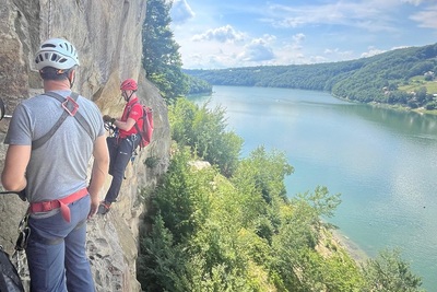 Na półce skalnej pionowej skały do wspinaczki, na linach wspinają sie funkcjonariusz SG i ratownik GOPR. na głowach mają kaski i wyposażeni są w niezbędny sprzęt wspinaczkowy. W tle widać taflę jeziora rożnowskiego i pogórze rożnowskie