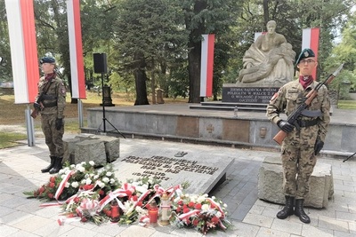 warta honorowa złożona z żołnierzy (kobieta i mężczyzna) pod pomnikiem nieznanego żołnierza w nowym Sączu. widoczne są również flagi białoczerwone oraz kwiaty i wieńce złożone pod pomnikiem.