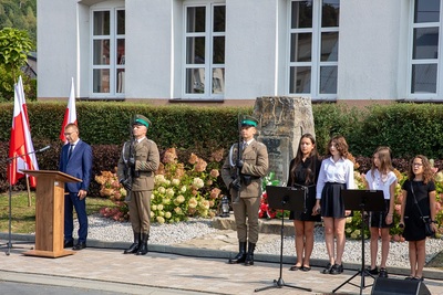 na zdjęciu widoczne są dzieci oraz prowadzący uroczystość upamiętniającą wybuch II wojny światowej. widoczni są  także funkcjonariusze straży granicznej którzy wystawili wartę honorową w tle powiewają flagi białoczerwone.