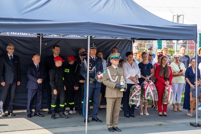 funkcjonariusz straży granicznej trzyma w ręku znicz pamięci który złoży pod pomnikiem podczas uroczystości z okazji wybuchy II wojny światowej. w tle widoczni pozostali uczestnicy trzymający wiązanki kwiatów w ręku.