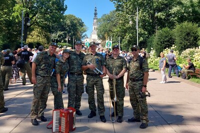 funkcjonariusze straży granicznej ubrani w mundury typu polo robiący sobie wspólne zdjęcie . w tle widoczna wieża sanktuarium na Jasnej Górze w Częstochowie. przed funkcjonariuszami postawiony jest akordeon.