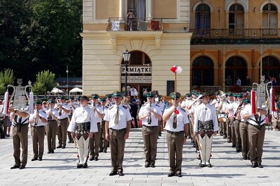 orkiestra reprezentacyjna stojąca na baczność w szyku podczas uroczystości. ubrani są w białe służbowe koszule i spodnie koloru khaki. przed nimi stoi zastępca naczelnika i tamburmajor orkiestry.