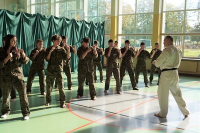 uczniowie klasy mundurowej o profilu straż graniczna wykonują ćwiczenia z samoobrony. prowadzi je funkcjonariusz straży granicznej ubrany w kimono karate w kolorze białym z czarnym pasem.