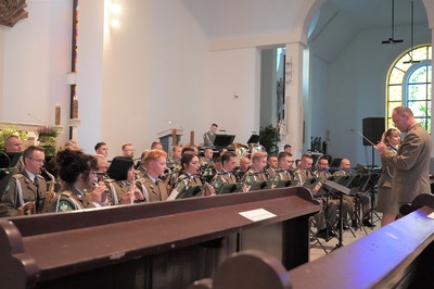 orkiestra reprezentacyjna straży granicznej podczas koncertu charytatywnego. przed orkiestrą dyryguje jej kapelmistrz. wszyscy ubrani są w mundur wyjściowy w kolorze khaki. koncert odbywa się w kościele.