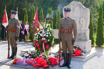 warta honorowa stojąca przy pomniku. pod pomnikiem złożone są wiązanki oraz kwiaty w kolorze białoczerwonym.