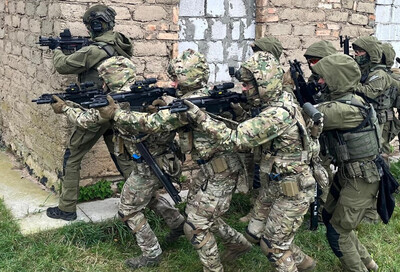 funkcjonariusze straży granicznej wykonujący ćwiczenia przy budynku na poligonie wojskowym. na zdjęciu widoczni funkcjonariusze podchodzący pod budynek w zwartej grupie. są wyposażeni w broń i umundurowani na bojowo.