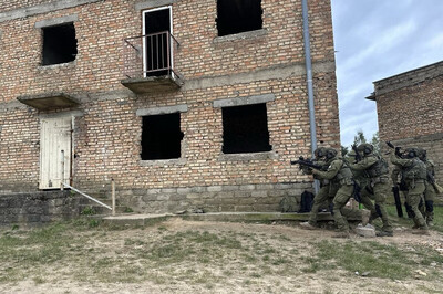 funkcjonariusze straży granicznej wykonujący ćwiczenia przy budynku na poligonie wojskowym. na zdjęciu widoczni funkcjonariusze podchodzący pod budynek w zwartej grupie. są wyposażeni w broń i umundurowani na bojowo.