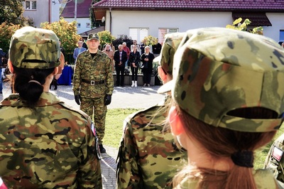 na zdjęciu widoczny funkcjonariusz straży granicznej który jednocześnie prowadzi zajęcia w szkole z uczniami klas mundurowych a na uroczystości jest dowódcą uroczystości. w tle widoczni zebrani ludzie.