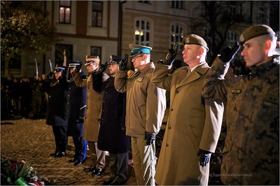 komendant placówki straży granicznej w Kielcach oddaje honor wraz z innymi przedstawicielami służb mundurowych przed pomnikiem podczas uroczystości z okazji święta niepodległości. W tle widoczni inni uczestnicy uroczystości.