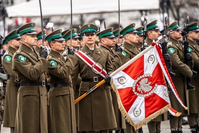 funkcjonariusze straży granicznej podczas uroczystości z okazji święta niepodległości w warszawie. na pierwszym planie widoczny funkcjonariusz trzymający w rękach sztandar straży granicznej. obok nie funkcjonariusze trzymający szable na baczność. w tle reszta funkcjonariuszy stojących w szyku i trzymających w ręku karabiny.