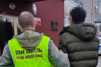 przed wejściem do budynku w którym mieści się placówka sg w kielcach funkcjonariusz w kamizelce z napisem straż graniczna polish border guard prowadzi zatrzymanego obywatela kolumbii