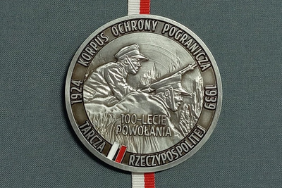 na zdjęciu widoczny medal z okazji stu lecia powołania korpusu ochrony pogranicza. jest koloru srebrnego z białoczerwona wstawką. medal przedstawia żołnierzy korpusu ochrony pogranicza prawdopodobnie podczas walki. na tym obrazie jest napis stu lecie powołania. na okrągłej krawędzi medalu znajduje się napis Korpusu ochrony pogranicza, następnie rok 1939 po jej przeciwległej stronie rok 1924 a na dole medalu napis tarcza rzeczypospolitej. medal umieszczony jest w reprezentacyjnym etui z białoczerwoną wstążką.