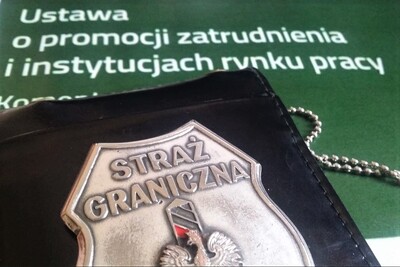 Odznaka funkcjonariusza straży granicznej leży na wydrukowanej ustawie o promocji zatrudnienia i rynku pracy