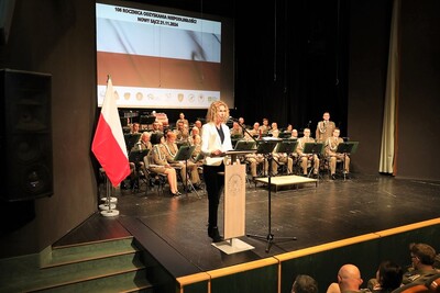 Na scenie na tle barw narodowych w imieniu Wojewody Małopolskiego odczytuje jego życzenia kobieta  - Zastępca Dyrektora Biura Wojewody Małopolskiego.