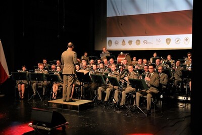 Widok Orkiestry Reprezentacyjnej wykonującej utwór muzyczny wraz z dyrygentem.