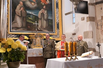 wnętrze kościoła w tropiu. przy ołtarzu kapelan kaosg, oraz towarzyszących mu dwóch funkcjonariuszy KaOsg oraz lektor - pracownik KaOSG. na ołtarzu przykrytym białym obrusem leży  ewangeliarz, trzy zapalone świece i krzyż. w rogu po lewej stronie żółte chryzantemy w doniczce. w tle tabernakulum oraz obraz w ołtarzu głównym  na którym widać św. Świętych Pustelników Andrzeja Świerada i Benedykta pod krzyżem