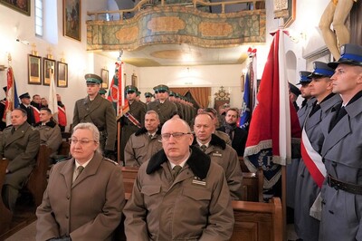 wnętrze kościoła w tropiu. uczestnicy mszy siedzą w ławkach. między ławkami stoi kompania reprezentacyjna sg, po bokach poczty sztandarowe policji, służby więziennej państwowej straży pożarnej i gopru