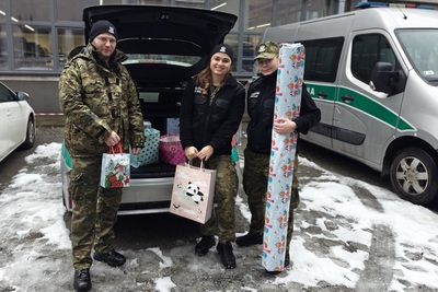 dwie funkcjonariuszki i funkcjonariusz stoja na parkingu przed otwartym bagażnikiem, w którym znajdują się zakupione prezenty dla domu dziecka. w rękach trzymają również zakupione prezenty