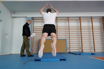 kandydat wykonuje ćwiczenie podczas egzaminu ze sprawności fizycznej. obok stoi funkcjonariusz straży granicznej.  egzamin odbywa się w hali sportowej karpackiego oddziału straży granicznej.