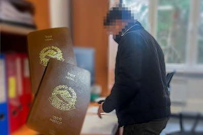 Osoba zatrzymana z zamazaną twarzą stoi nad biurkiem, podpisuje dokumenty w pomieszczeniach straży Granicznej, po lewej stronie zdjęcia wklejona miniaturka paszportu obywatela Nepalu