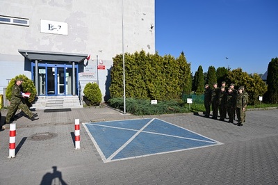 funkcjonariusze straży granicznej stoją na uroczystej zbiórce patrząc na poczet flagowy, w tle widać budynek straży Granicznej