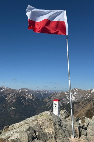 flaga polski na maszcie, łopocząca na wietrze w tle widać góry