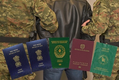 Kolaż zdjęć. Na tle prowadzonego pod ręce przez dwóch funkcjonariuszy zatrzymanego cudzoziemca znajduje się 5 paszportów zatrzymanych cudzoziemców. Są to od lewej: dwa paszporty indyjskie, następnie azerski, kolumbijski i bengalski.