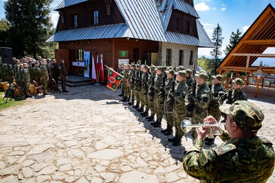 Polana przed schroniskiem na przehybie. po prawej stronie Stoi na baczność kompania reprezentacyjna straży granicznej, w kaplicy którą widać przez otwarte na oścież drzwi odprawiana jest msza święta. Przed kaplicą siedzą uczestnicy mszy świętej polowej