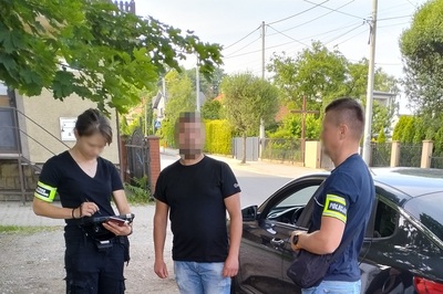 funkcjonariuszka straży granicznej oraz funkcjonariusz policji legitymują cudzoziemca stojącego przy samochodzie. Funkcjonariusze są w ubraniu cywilnym, na ramionach mają odblaskowe opaski z napisem straż graniczna i policja. cudzoziemiec ma zapikselizowaną twarz