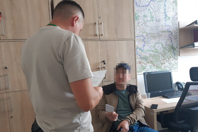 Zatrzymany cudzoziemiec w kajdankach siedzi na krześle w pomieszczeniu biurowym straży granicznej. pilnuje go nieumundurowany funkcjonariusz. cudzoziemiec ma zapikselizowaną twarz