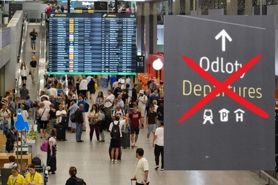 Widok z góry na halę ogólnodostępną krakowskiego lotniska, widać setki podróżnych z walizkami i plecakami.. Na to po prawej nałożone zdjęcie z napisem odloty, przekreślone czerwonym krzyżykiem.