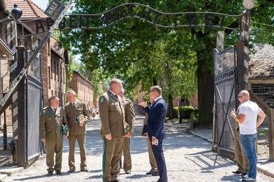 Funkcjonariusze straży granicznej i mężczyzna ubrany w niebieski garnitur oraz mężczyzn w białej koszulce stoją w branie obozu koncentracyjnego Auschwitz