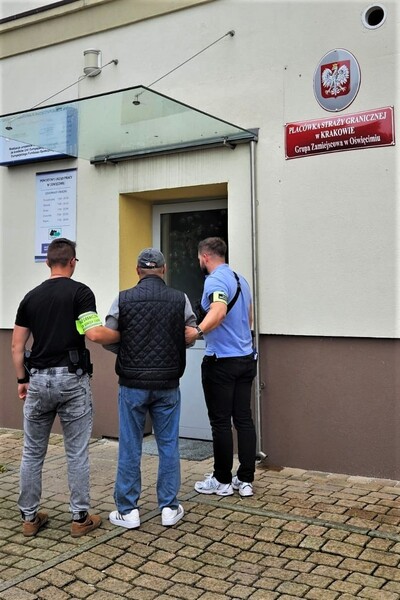 dwóch funkcjonariuszy straży granicznej prowadzący zatrzymanego do pomieszczeń służbowych straży granicznej
