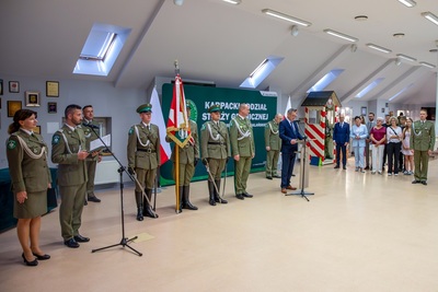 Na zdjęciu widać grupę osób ubranych w mundury galowe. Widoczny jest poczet sztandarowy wraz z sztandarem. Po prawej stronie widać grupę osób cywilnych.