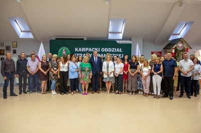 Grupa osób stoi na środku pomieszczenia. Za nimi znajduje si e duży zielony baner z napisem białymi literami.