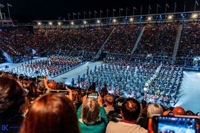 Na zdjęciu prezentacje orkiestr reprezentacyjnych formacji mundurowych z różnych krajów. Orkiestry prezentują się na scenie, w rękach instrumenty dęte. Muzycy mają na sobie umundurowanie charakterystyczne dla danej formacji. w tle widoczna publiczność.