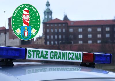 Na zdjęciu w tle Zamek Królewski w Krakowie. Na pierwszym planie fragment dachu samochodu służbowego wyposażonego w  niebiesko-czerwone sygnały świetlne (tzw. koguty), pomiędzy nimi napis Straż Graniczna. Po lewej stronie w rogu logotyp Karpackiego Oddziału Straży Granicznej w Nowym Sączu
