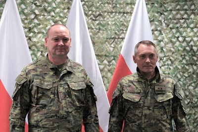 Dwóch funkcjonariuszy stoi na tle białoczerwonych flag