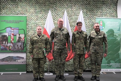w szeregu stoi 4 funkcjonariuszy w tle flagi biało czerowne i rolupy jednostek