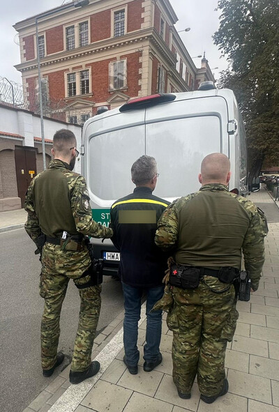 Zatrzymany cudzoziemiec prowadzony przez dwóch funkcjonariuszy wyprowadzany jest z busa typu więźniarka pod aresztem śledczym w Krakowie.