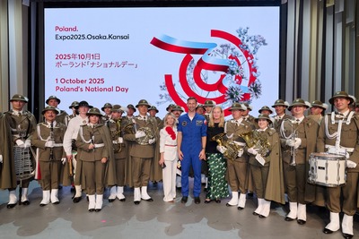 Pamiątkowe zdjęcie delegacji, orkiestry i astronauty przed ekranem z napisem &quot;Poland&#039;s National Day, Expo 2025.Osaka.Kansai&quot;.