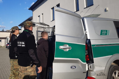 Dwaj funkcjonariusze straży granicznej wprowadzają do samochodu sg typu więźniarka zatrzymanego obywatela ukrainy.