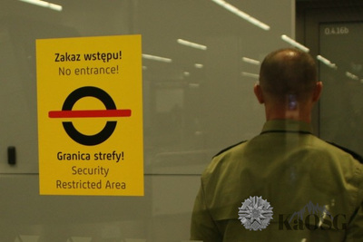 Na zdjęciu widać szklane drzwi, na których jest informacja  o zakazie wstępu. Za drzwiami stoi mężczyzna  widoczny tyłem w zielonej koszuli.